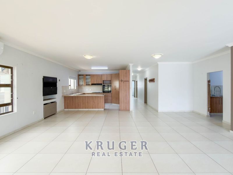Spacious open-plan living area featuring large format floor tiles, a modern kitchen with built-in appliances, and an integrated air conditioning unit.