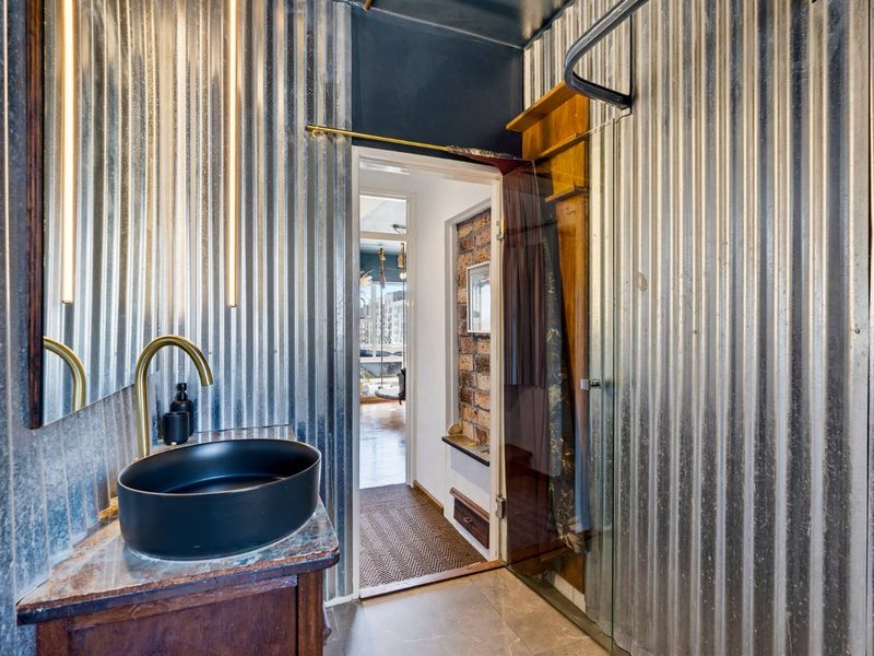Modern industrial-style bathroom featuring corrugated metal wall cladding, a sleek vessel sink with brass fixtures, and a glass-enclosed shower area.