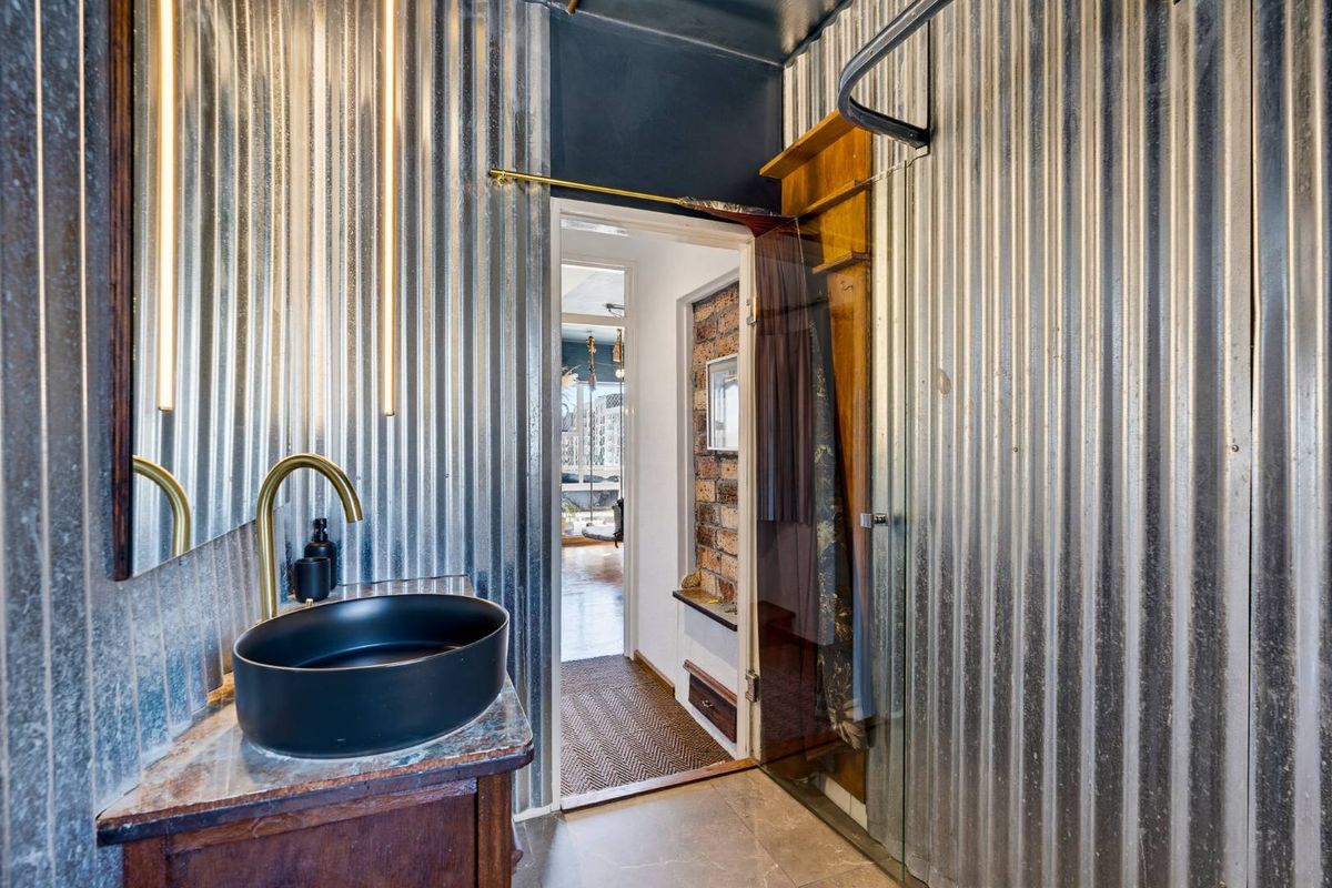 Modern industrial-style bathroom featuring corrugated metal wall cladding, a sleek vessel sink with brass fixtures, and a glass-enclosed shower area.
