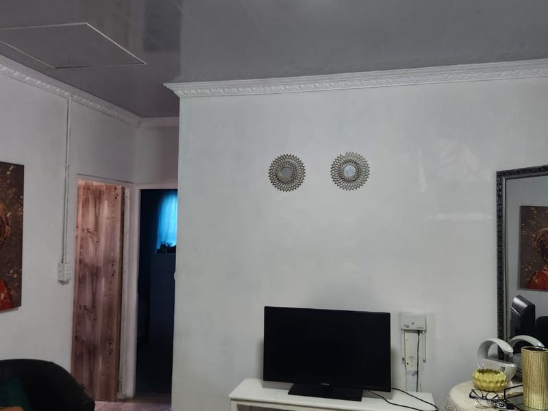 A living room area featuring tiled flooring, ceiling cornicing, and a central flush mount light fixture.