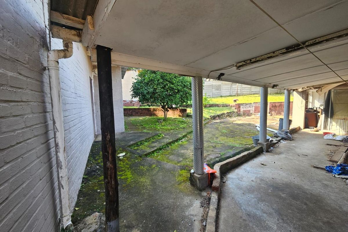 A covered outdoor patio area featuring concrete flooring and support columns, requiring maintenance and cleaning to restore the exterior space.