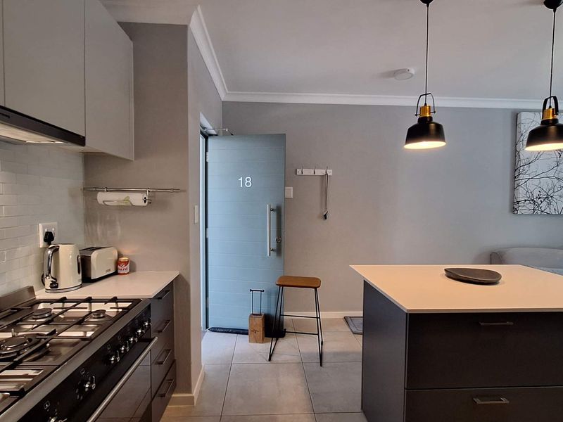 Modern open-plan kitchen and living area featuring a gas cooktop, central island, and contemporary pendant lighting with neutral finishes.