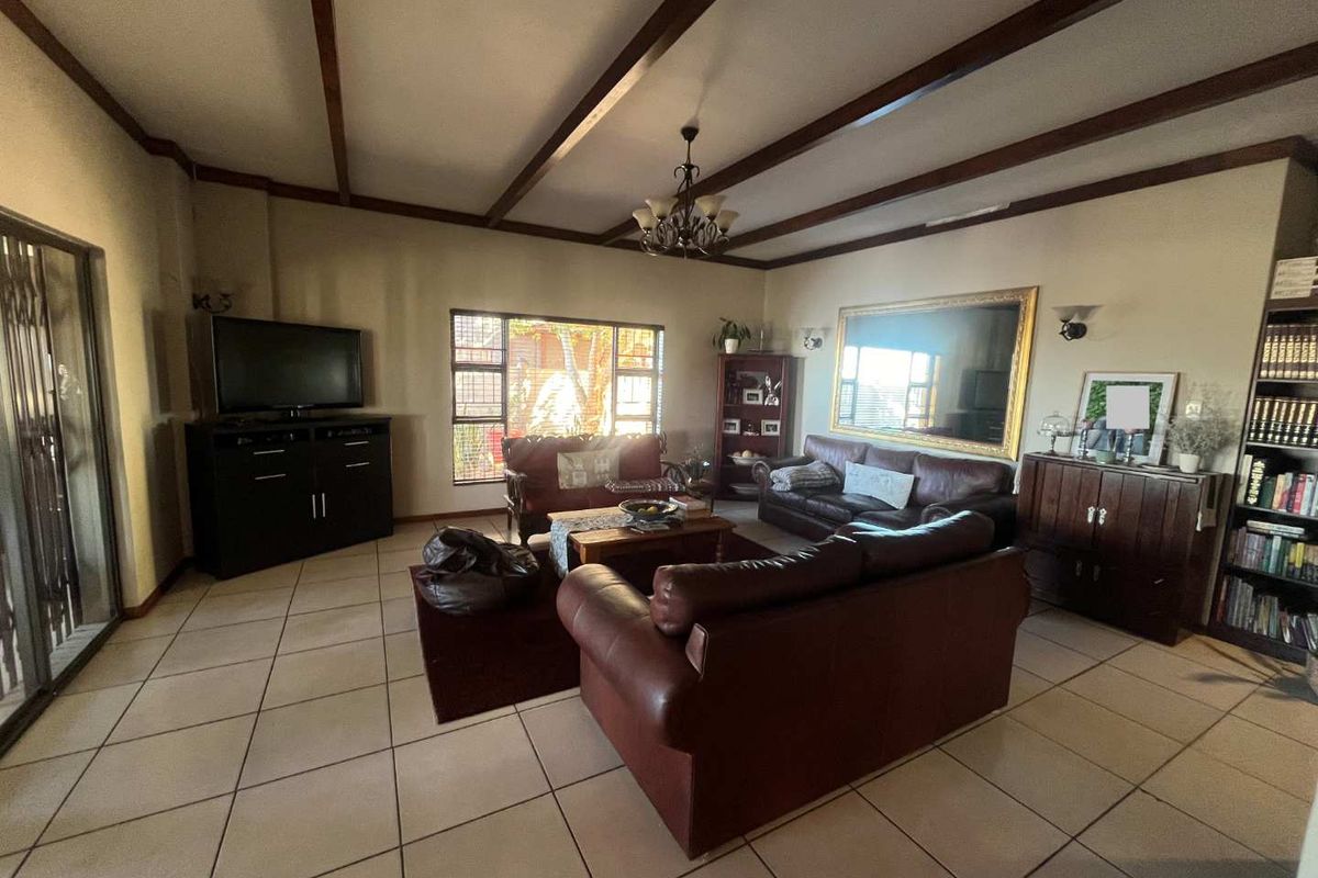 Spacious living room featuring exposed timber ceiling beams, tiled flooring, and large windows providing natural light.