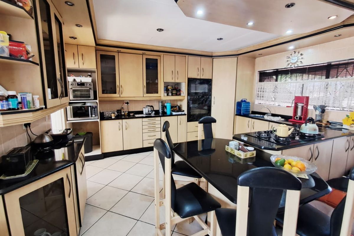 Spacious kitchen featuring light wood cabinetry, black granite countertops, integrated appliances, and a central dining area with tiled flooring.