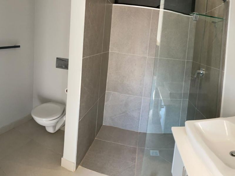 Modern bathroom featuring a glass-enclosed shower, wall-mounted toilet, and dual basin setup with contemporary tiling and fixtures.