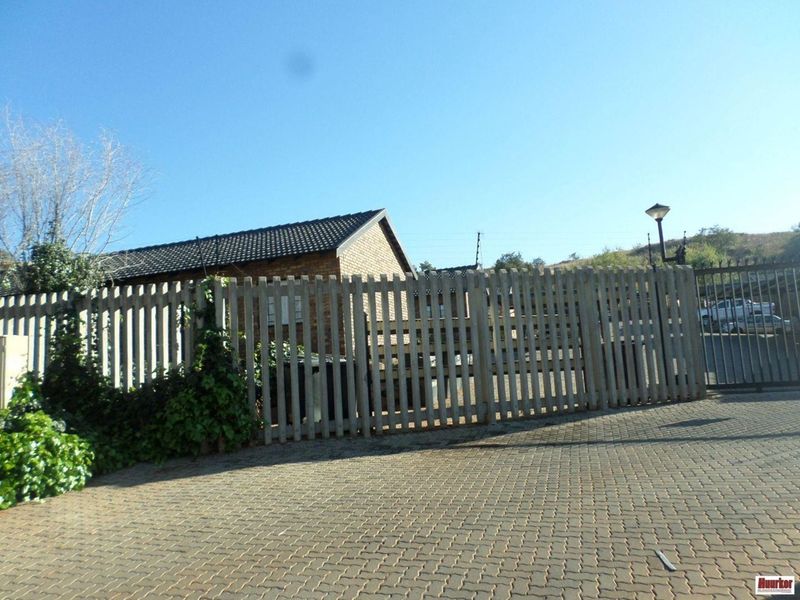 Front exterior view of the property featuring a paved driveway, secure picket fencing, and a brick building facade with a tiled roof.