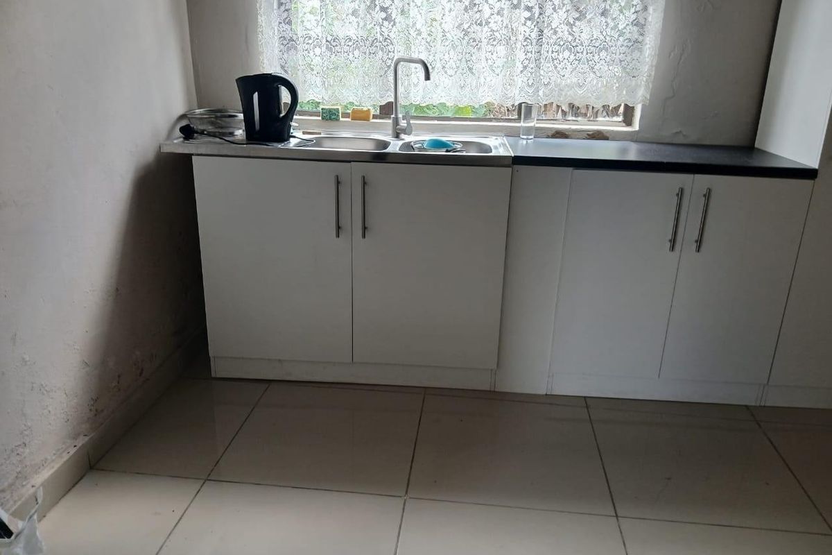 A compact kitchen area featuring white cabinetry, a stainless steel sink, and tiled flooring, requiring some wall maintenance and cosmetic updates.