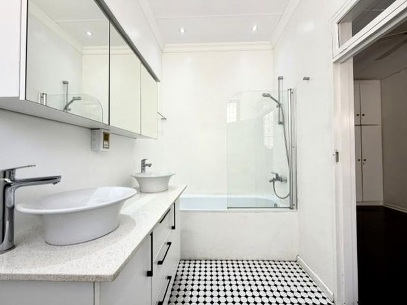 A clean, modern bathroom featuring a double vanity with vessel sinks, a built-in medicine cabinet, and a bathtub with a glass shower screen.