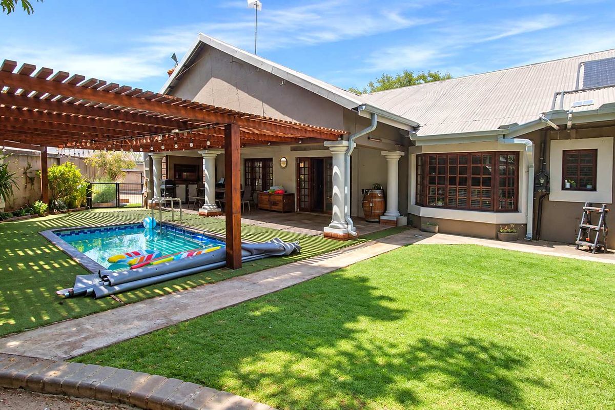 A well-maintained rear exterior featuring a swimming pool, a large wooden pergola, and a landscaped garden with a paved walkway.