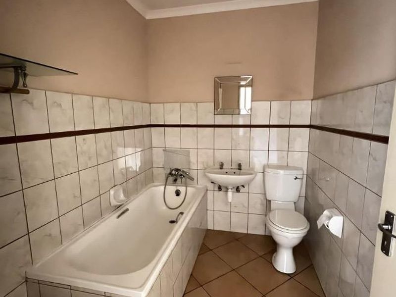 A functional bathroom featuring a bathtub, wall-mounted basin, and toilet with neutral ceramic tiling throughout.