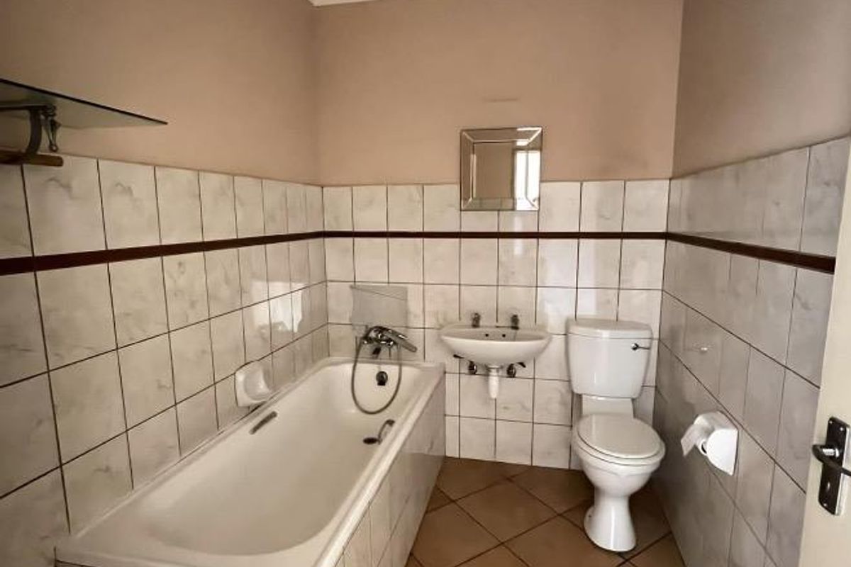 A functional bathroom featuring a bathtub, wall-mounted basin, and toilet with neutral ceramic tiling throughout.