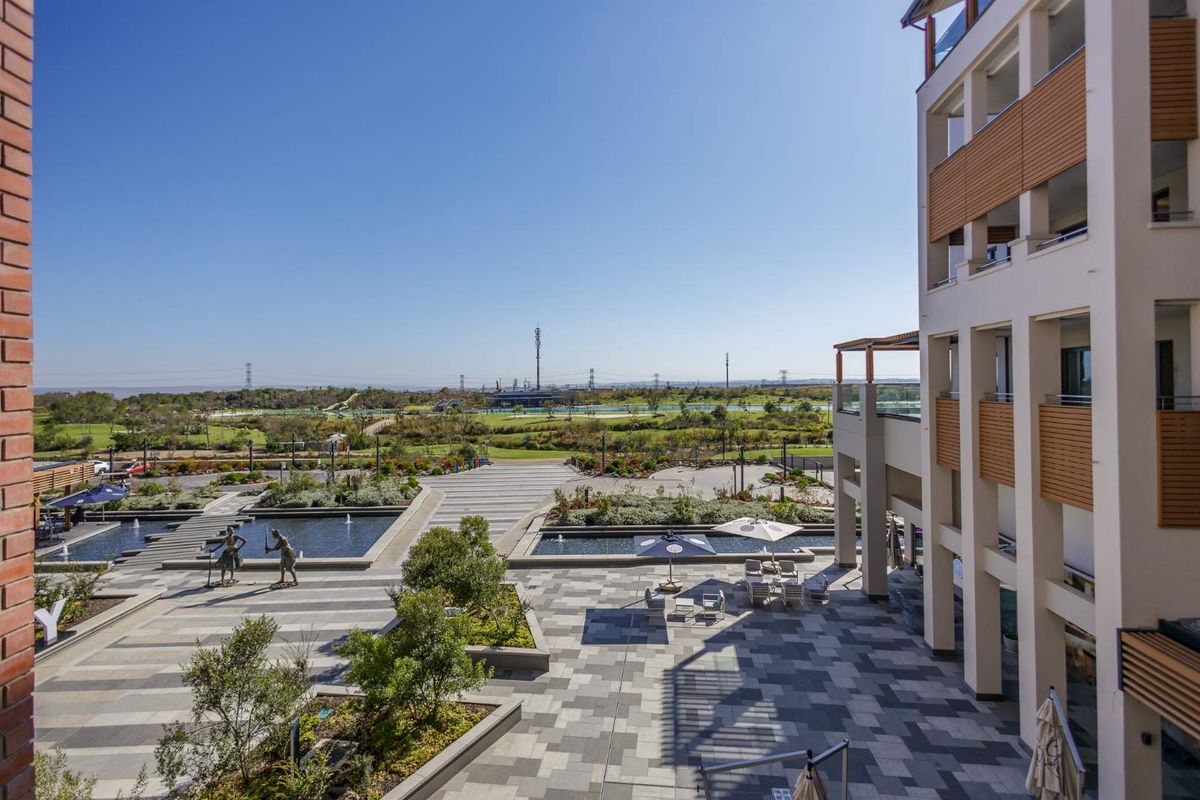 Elevated view of a modern apartment complex courtyard featuring paved walkways, water features, and landscaped gardens with a scenic outlook.