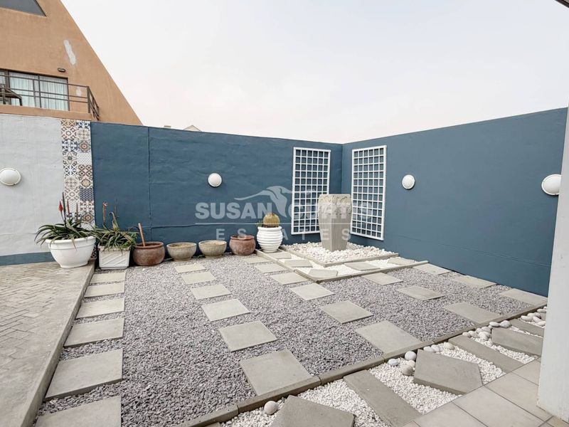 A landscaped rear courtyard featuring a stone water feature, gravel pathways, decorative wall panels, and modern exterior wall lighting.
