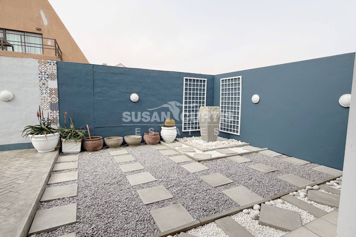 A landscaped rear courtyard featuring a stone water feature, gravel pathways, decorative wall panels, and modern exterior wall lighting.