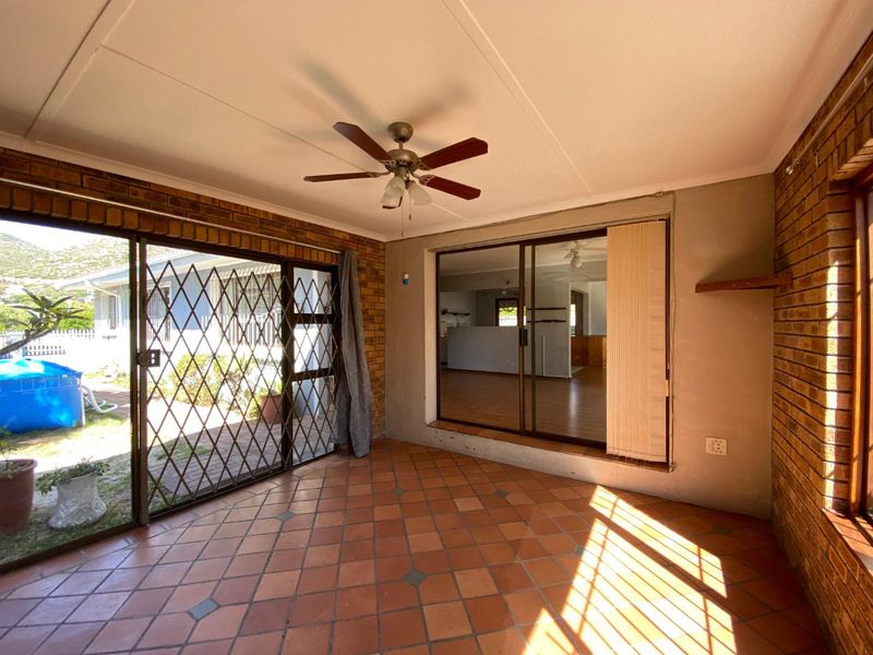 A covered patio area featuring terracotta tile flooring, exposed brick walls, and sliding glass doors providing access to the garden and interior living space.