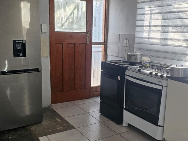 A functional kitchen area featuring tiled flooring, a gas stove, and an external timber door with access to the exterior.