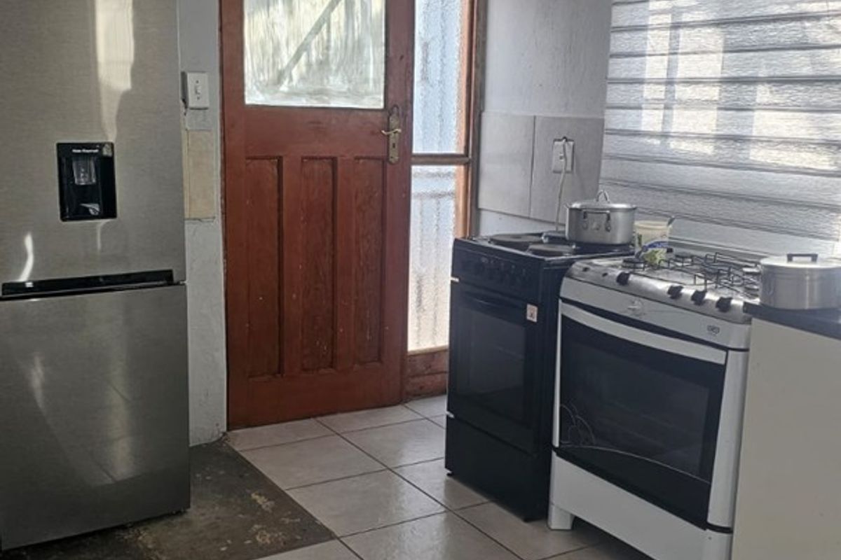 A functional kitchen area featuring tiled flooring, a gas stove, and an external timber door with access to the exterior.