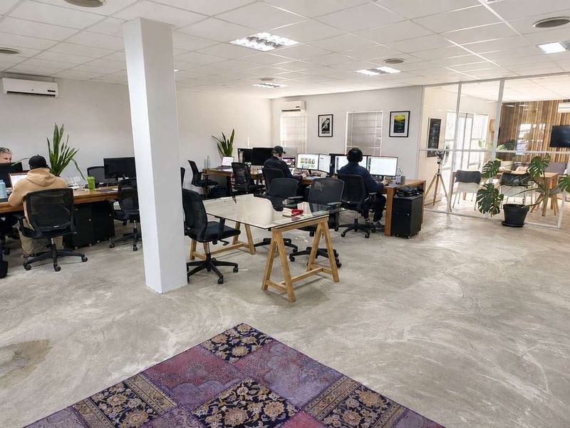 Open-plan office space featuring polished concrete floors, suspended ceilings with recessed lighting, and a glass-partitioned meeting area.