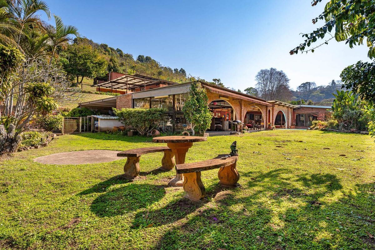A spacious rear exterior view featuring a large brick-built home with an expansive covered arched patio overlooking a well-established garden.