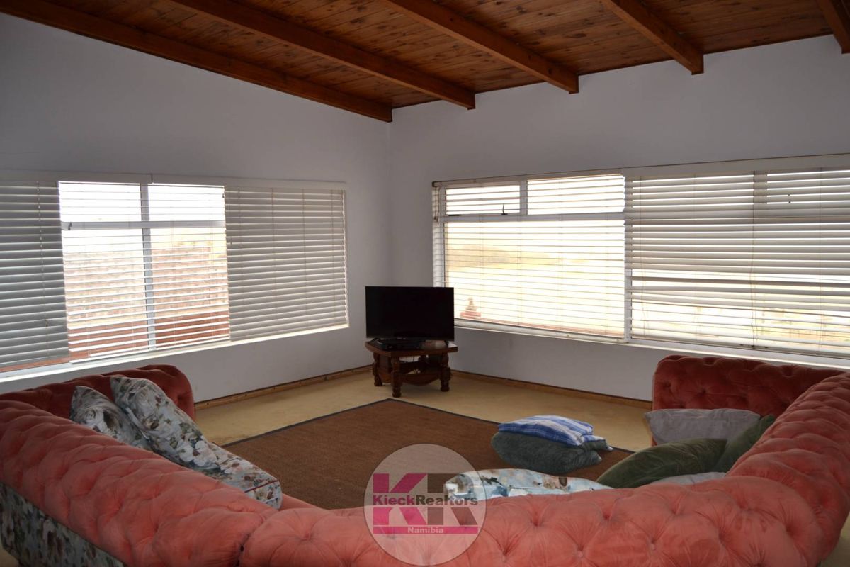 Spacious living room featuring an exposed timber beam ceiling and large windows with venetian blinds, offering a bright and open atmosphere.