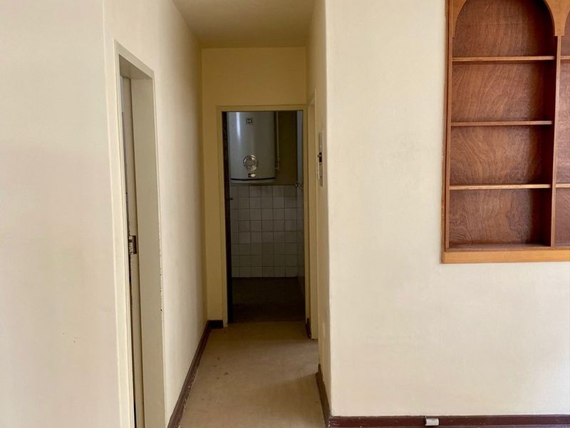 A vacant hallway featuring built-in wooden shelving and access to a utility area containing an electric water heater.