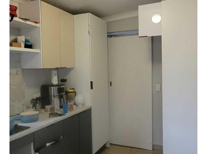 A compact kitchen area featuring two-tone cabinetry, tiled flooring, and a sliding door, currently requiring minor repairs and finishing touches.