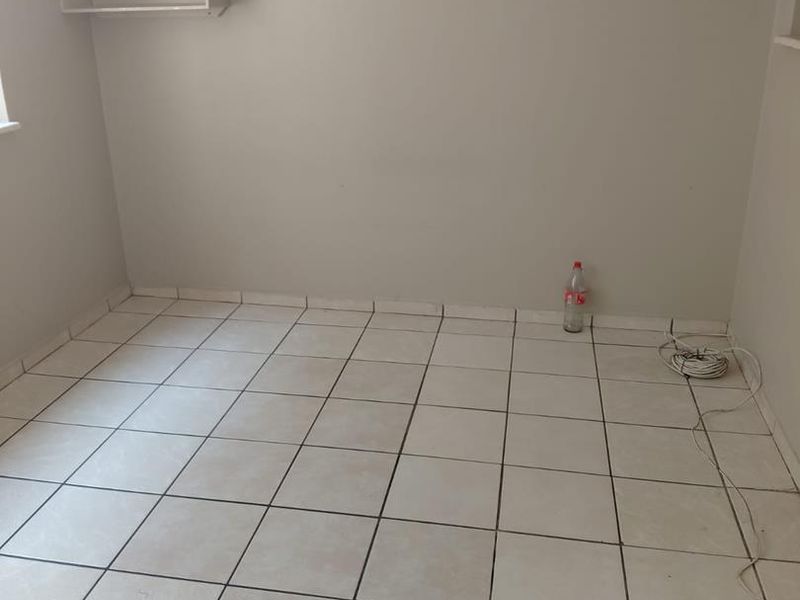 An empty bedroom featuring tiled flooring and a wall-mounted shelf, presenting a blank canvas for potential interior design updates.