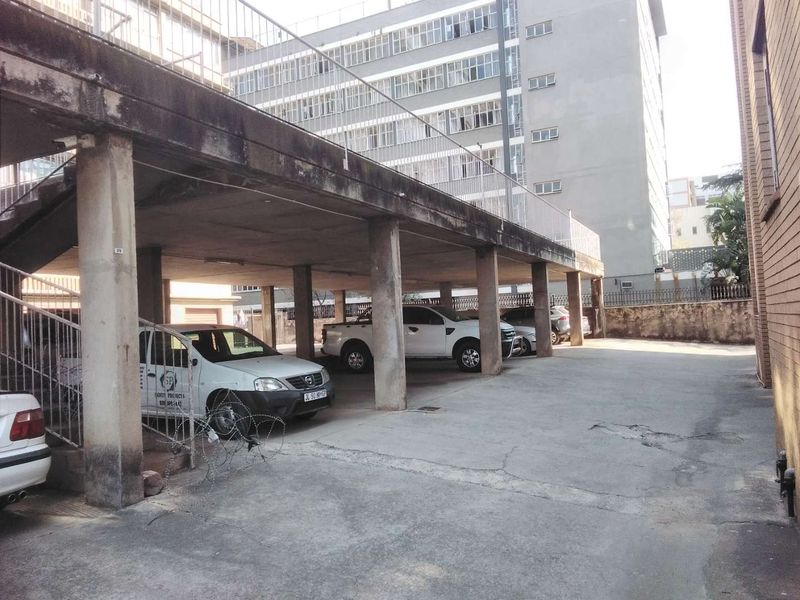 Covered parking area featuring concrete pillars and a concrete slab ceiling, providing sheltered vehicle storage for the apartment complex.