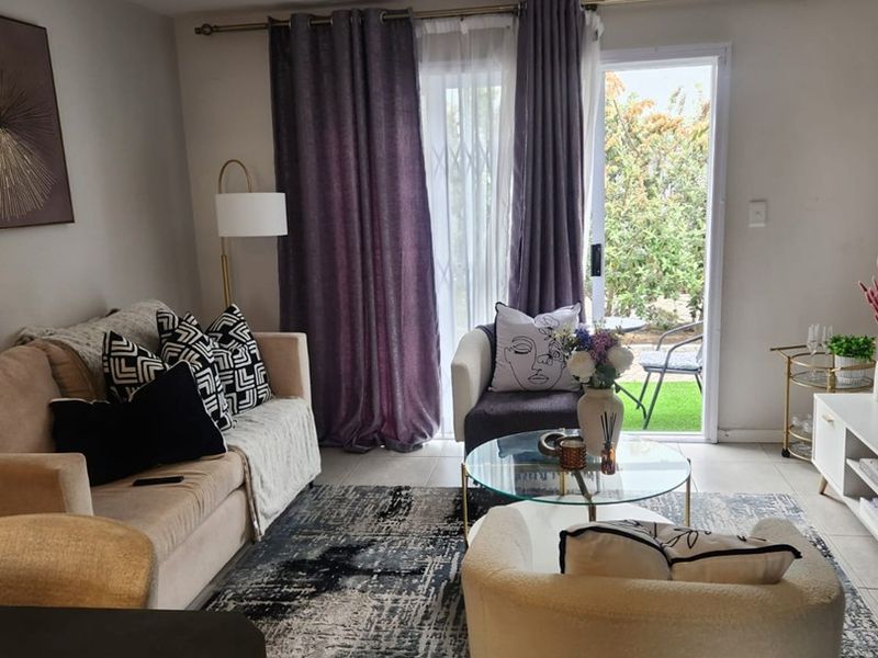 A well-lit living room featuring tiled flooring and a sliding glass door with a security gate, providing direct access to an outdoor area.