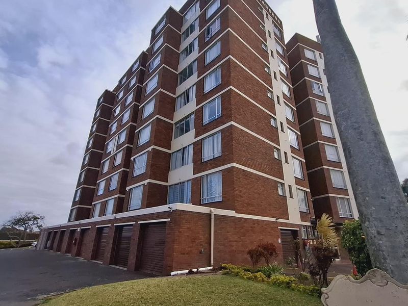 A low-angle view of the Orchid Gardens apartment building, featuring a classic brick facade, ground-level garage access, and surrounding landscaped grounds.