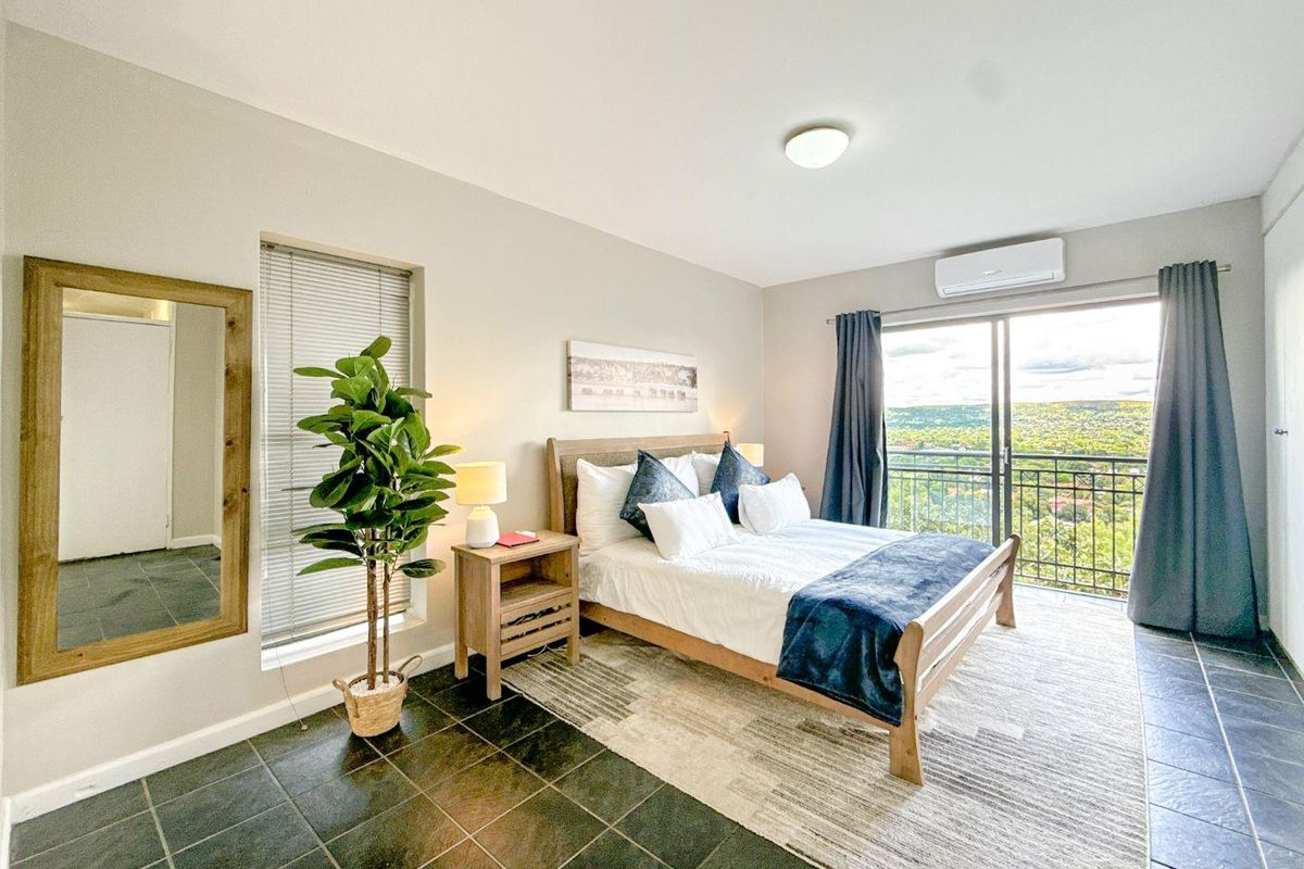 A well-maintained bedroom featuring tiled flooring, a split-system air conditioner, and a sliding glass door leading to a balcony with scenic views.