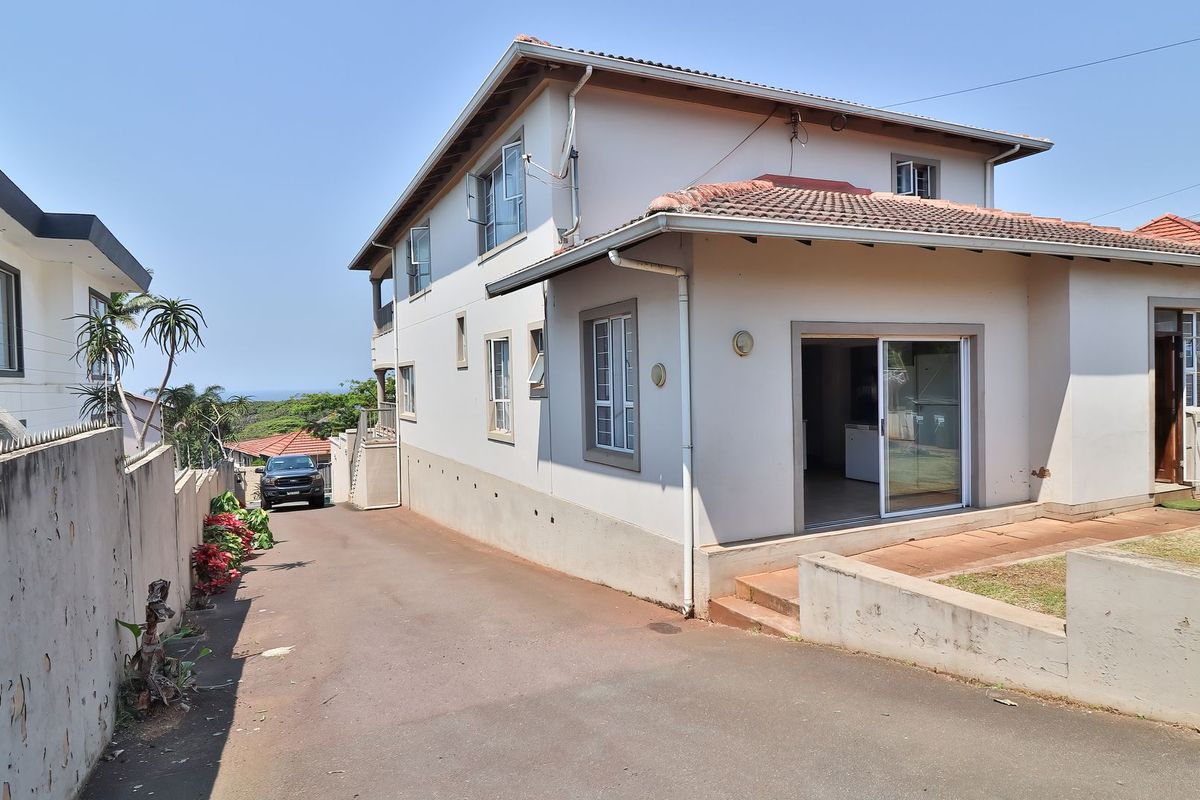 Rear view of the property featuring a concrete driveway, tiled roof, and sliding door access to the interior.