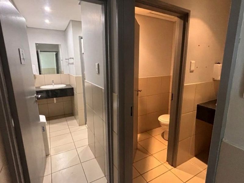 A functional office bathroom facility featuring tiled flooring, granite-topped vanity basins, and separate toilet cubicles with neutral wall tiling.