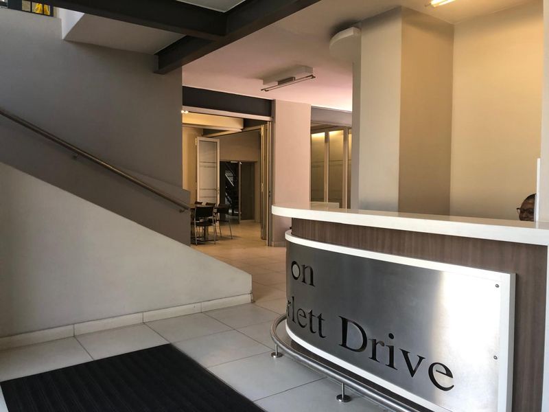 Modern office building entrance featuring a professional reception desk, tiled flooring, and a staircase leading to upper levels.