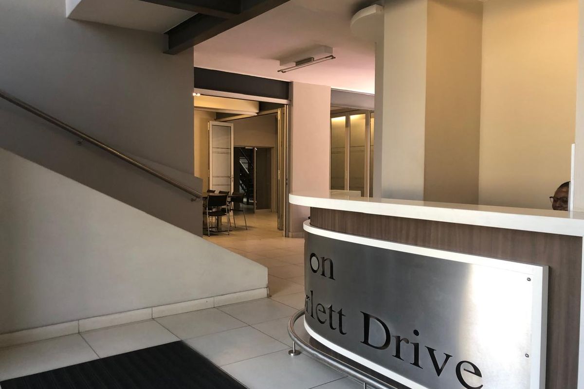 Modern office building entrance featuring a professional reception desk, tiled flooring, and a staircase leading to upper levels.