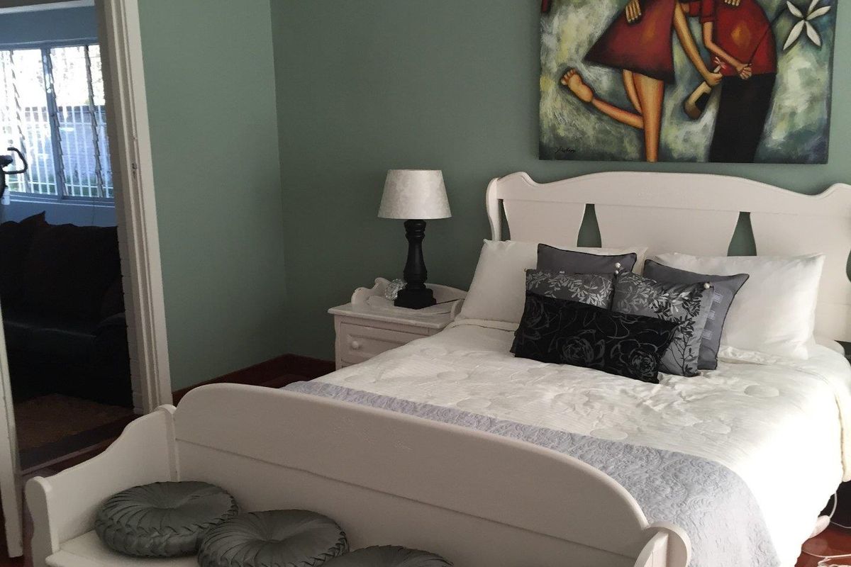 A bedroom featuring painted walls and timber flooring, with an adjacent room visible through the doorway.