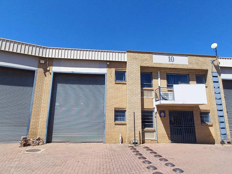 Industrial unit exterior featuring multiple roller shutter doors, face brick facade, and a paved driveway entrance.
