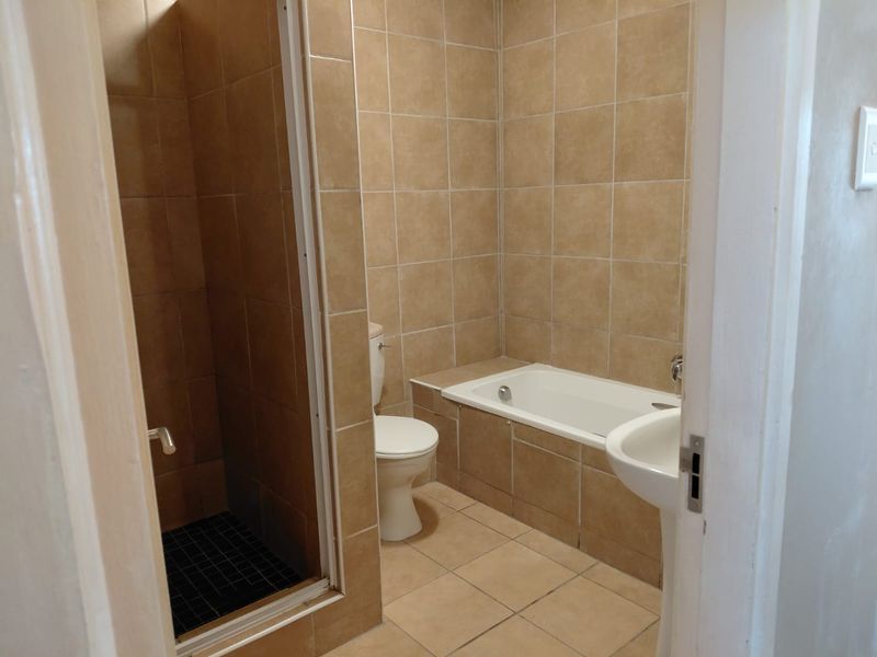 A functional bathroom featuring a built-in bathtub, separate shower enclosure, pedestal sink, and neutral floor-to-ceiling tiling.