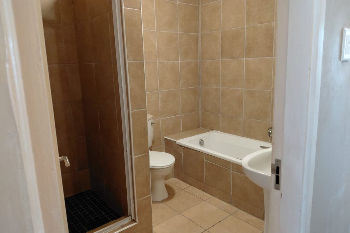 A functional bathroom featuring a built-in bathtub, separate shower enclosure, pedestal sink, and neutral floor-to-ceiling tiling.