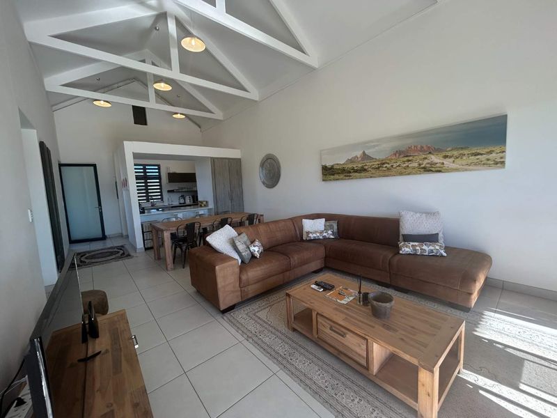 Spacious open-plan living and dining area featuring high vaulted ceilings with exposed trusses, tiled floors, and an integrated kitchen space.