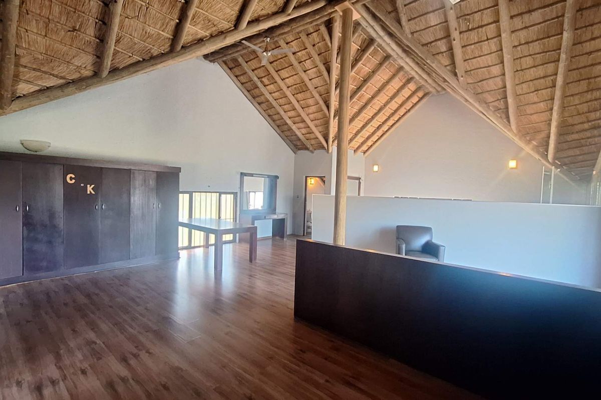 Spacious living area featuring high vaulted ceilings with exposed timber trusses, thatched roofing, and laminate flooring, offering a versatile open-plan layout.