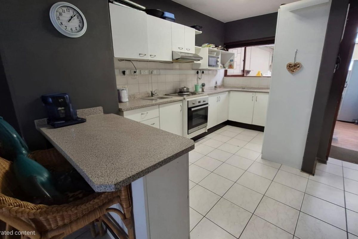 A functional kitchen featuring white cabinetry, laminate countertops, built-in oven, extractor fan, and tiled flooring with an integrated breakfast bar.