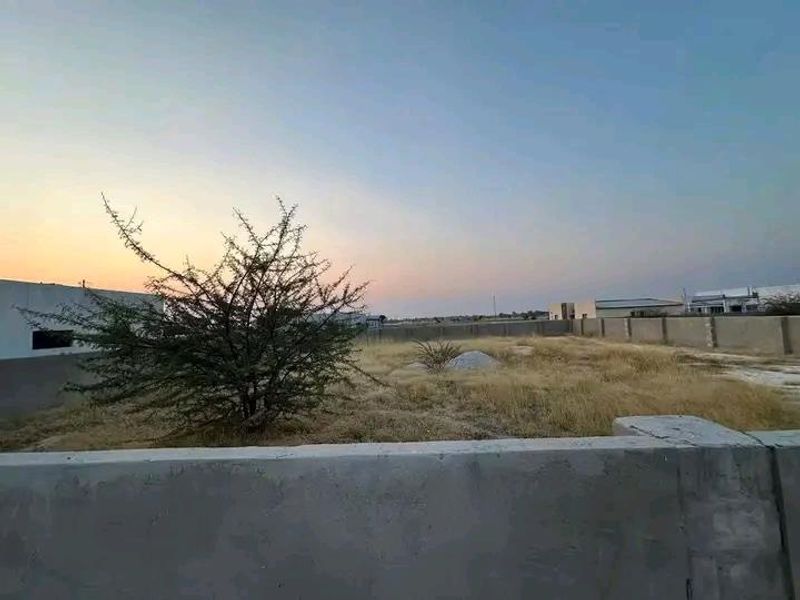 A view of a vacant commercial land plot featuring a concrete perimeter boundary wall and natural vegetation.