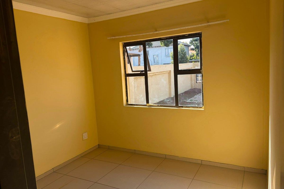 A vacant bedroom featuring tiled flooring, yellow painted walls, and a metal-framed window providing natural light.