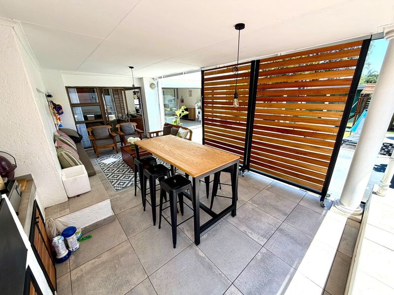 A spacious covered patio featuring large format floor tiles, a built-in braai, and a modern timber privacy screen, perfect for outdoor entertaining.