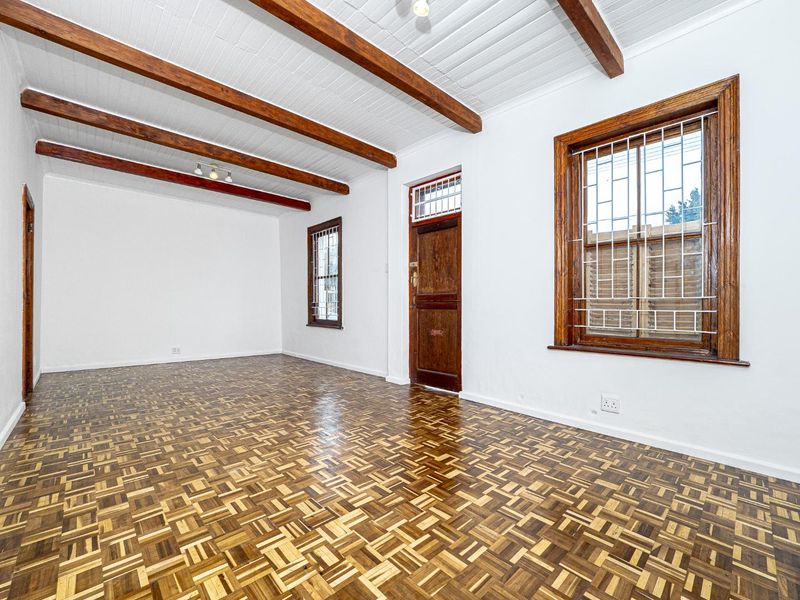 Spacious living area featuring classic parquet flooring, exposed timber ceiling beams, and large windows with security bars.