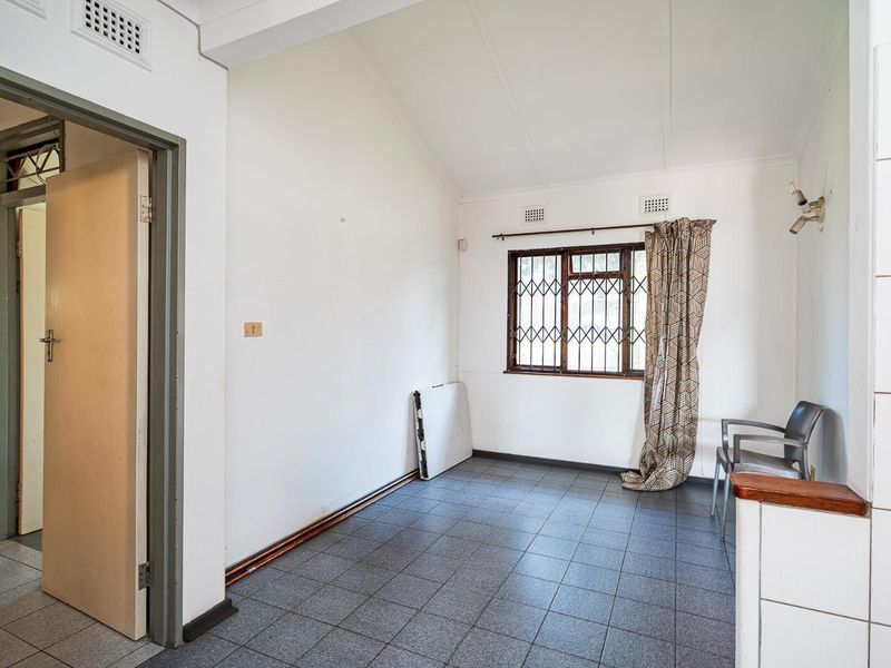 A vacant living area featuring tiled flooring, security bars on the window, and neutral wall finishes, offering a blank canvas for potential updates.