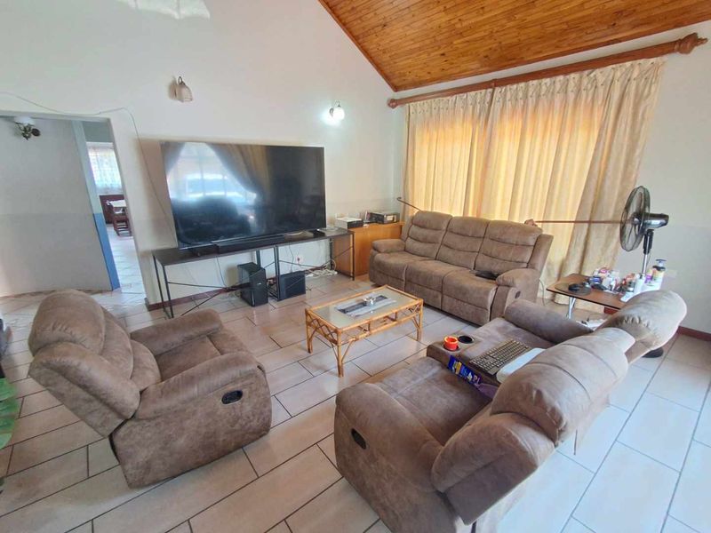 Spacious living room featuring a high vaulted timber ceiling and neutral ceramic floor tiles, offering a comfortable and well-lit area for relaxation.