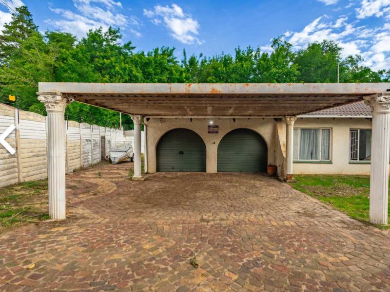 A double garage with an attached carport featuring decorative columns and a paved driveway, set against a precast boundary wall.