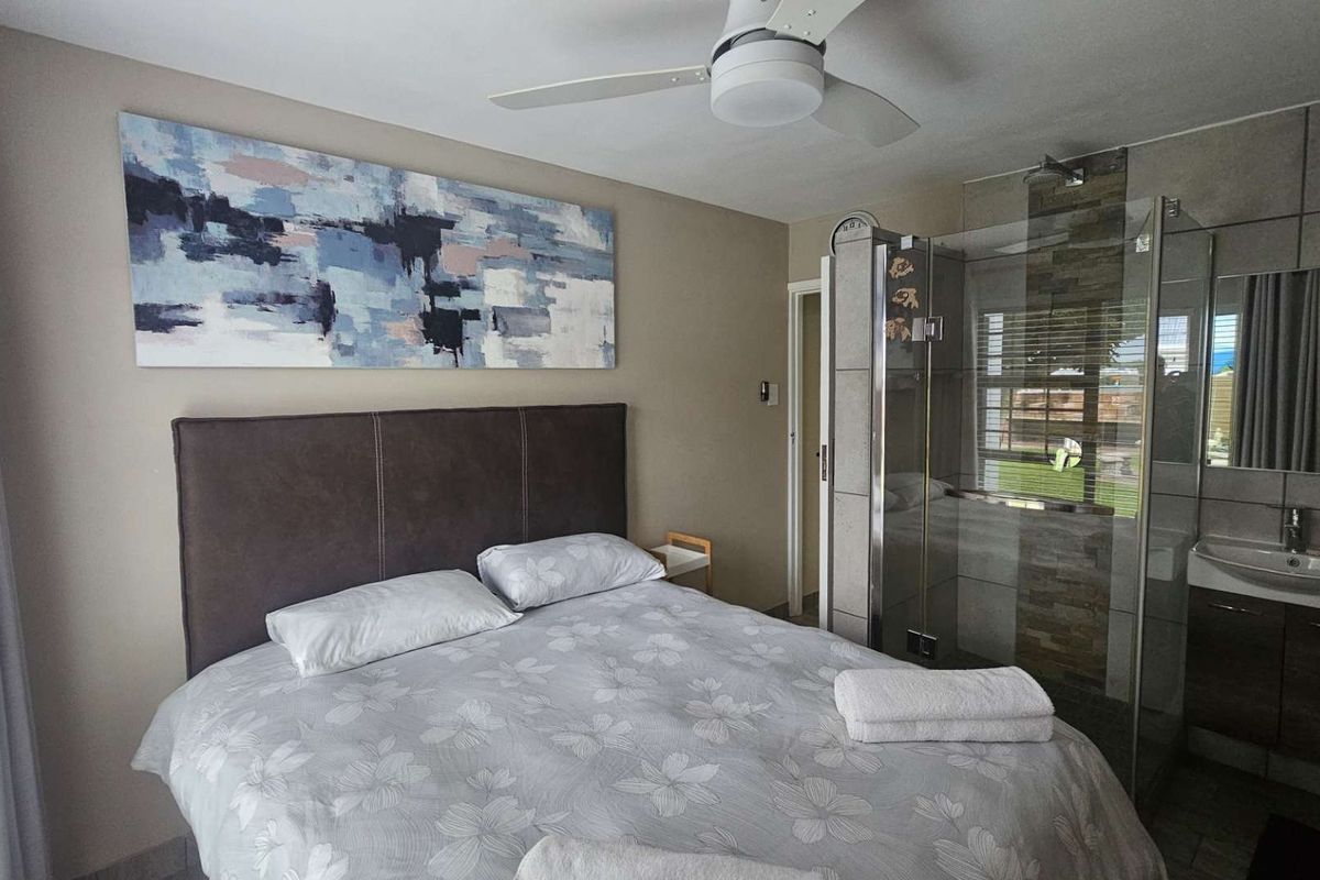 A well-maintained bedroom featuring an en-suite bathroom with a glass shower enclosure and modern vanity basin, complemented by a ceiling fan.